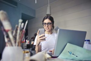 femme avec son téléphone dans la main et devant son ordinateur entrain de sourire